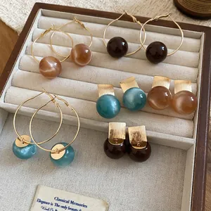 Set of resin marble hoop earrings and round studs in blue and brown on a beige tray