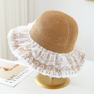 Detail of a brown straw sun hat featuring a delicate white lace brim and floral texture
