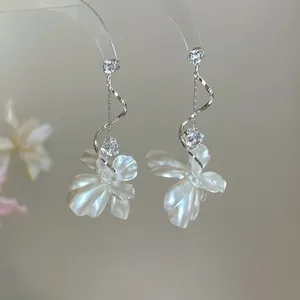 Détail de boucles d'oreilles pendantes avec pétales blancs, spirales et zircons clairs
