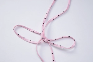 Detail of pink satin bikini bow with black polka dots on a clean white background