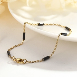 Détail du bracelet doré avec perles noires cylindriques et fermoir mousqueton sur plat blanc