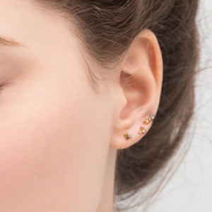 Close-up of gold stud earring set with multi-colored zirconia stones on model's ear