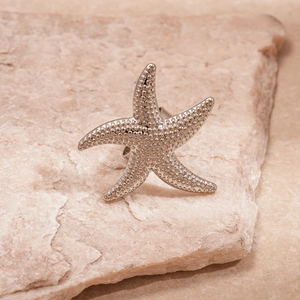 Macro shot of silver starfish ring with embossed texture on natural stone background