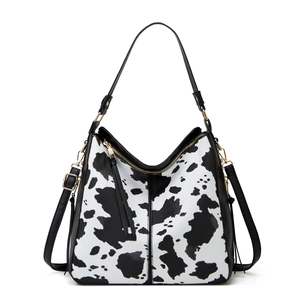 Detail of cow print tote bag with black handles, gold hardware, and tassel zipper puller