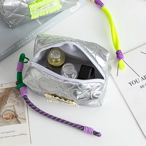 Détail d'une trousse à maquillage argentée matelassée avec coutures en cœur et anse