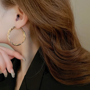Close-up profile of a model wearing large gold geometric hoop earrings in a minimalist style