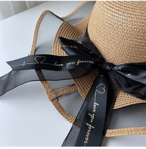 Detail of straw sun hat featuring mesh splicing and black ribbon with gold text