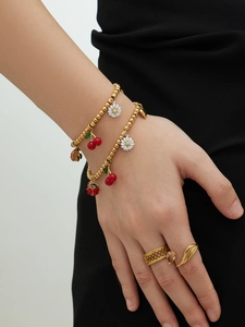Gros plan du bracelet à perles dorées avec breloques cerise, marguerite et coccinelle