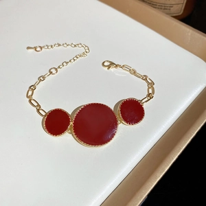 Vue à plat d'un bracelet chaîne doré avec trois pendentifs ronds rouges sur plateau