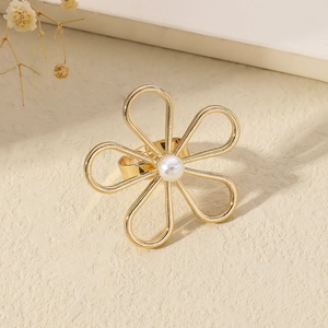 Gold flower ring with six petals and a white pearl center on a minimalist beige background