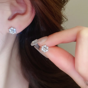 Close-up of sparkling zircon snowflake stud earrings shown on ear and held by hand