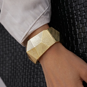Detail eines breiten goldenen geometrischen Armreifs mit Sonnenstrahl-Struktur