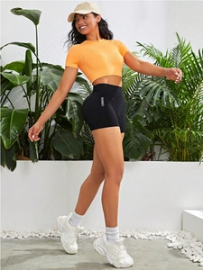 Outdoor-Fitness-Set mit orangefarbenem Crop-Top und schwarzen Shorts mit Seitenschrift