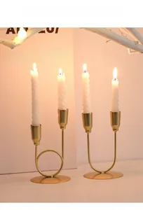 Détail d'un bougeoir en métal doré en forme de U avec bougie spirale blanche allumée