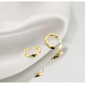 Detailed macro view of gold Mobius silver hoop earrings on a white silk background