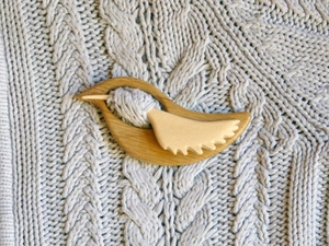 Detail of wooden bird brooch with pin fastening on a grey knitted sweater fabric