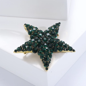 Detail view of gold pentagram brooch featuring deep green crystals on a minimalist platform