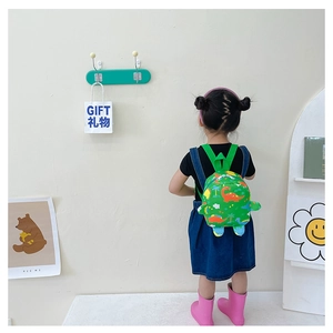 Rear view of a child wearing a green dinosaur cartoon backpack in a cozy room