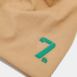 Detail of beige ribbed knit beanie featuring a high-contrast lime green 7th rubber logo