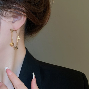 Close-up of gold hoop earrings with butterfly charms on female model in warm lighting