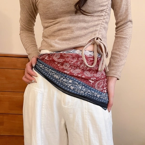 Detail of red and indigo paisley print scarf belt tied on white linen trousers