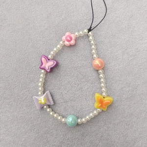 Detail of beaded phone strap with white pearls, colorful acrylic flowers and butterflies