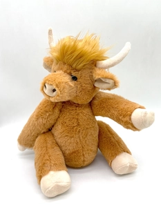 Close-up of brown plush Highland cow with long faux fur, white horns and a sitting pose