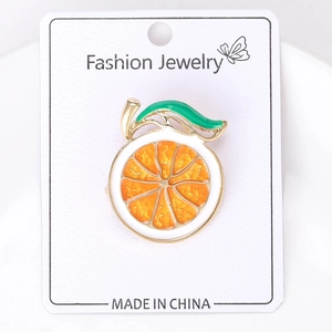 Detailed view of an enamel orange fruit brooch pinned on a Fashion Jewelry display card