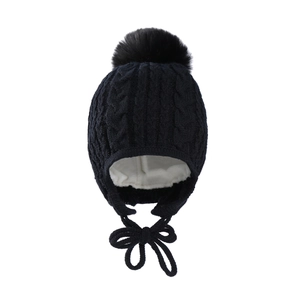 Close-up of black cable knit baby winter hat with pompom and earflaps on white background