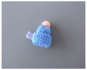 Detailed view of blue knitted mini hat hair clip with soft pink pom pom top
