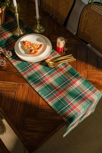 Close-up of a festive red and green plaid table runner on a wooden table with decorations