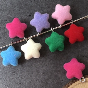 Colorful flocked star pendants with metal loops displayed on a textured stone surface
