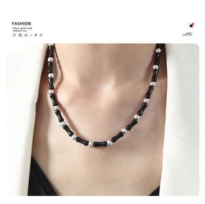 Detail of beaded necklace with black agate cylinders and silver beads on white suit