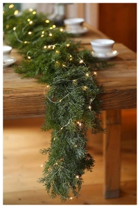 Detail view of realistic PE cypress garland with warm LED lights on a wooden table