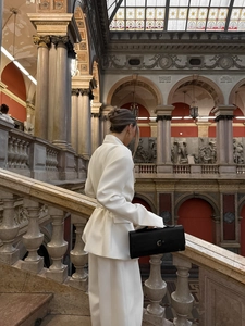 Detail of white cinched waist blazer and black leather handbag in elegant setting