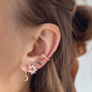 Close-up of gold moon and flower earrings set with green and white zircon stones