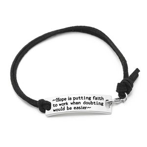 Detail of hand-woven black rope bracelet with engraved inspirational message metal plate