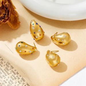 Detail of gold teardrop earrings with colorful zircon stones on vintage paper background