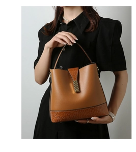 Detail of caramel leather bucket bag featuring crocodile texture and gold metal buckle