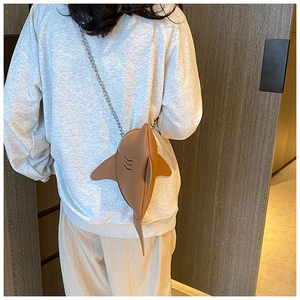 Detail of brown leather shark-shaped crossbody bag with silver chain strap on model