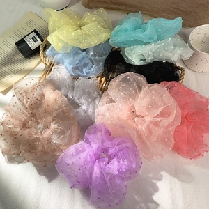 Detailed flat lay of colorful polka dot lace scrunchies on a soft white fabric background