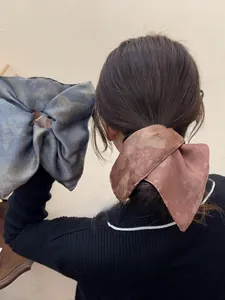 Close-up of oversized tie-dye bow scrunchies in blue-grey and reddish-brown silk fabric