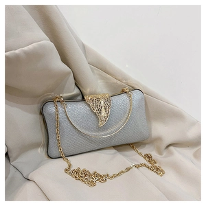 Close-up of silver glitter evening bag with golden leaf clasp on beige fabric