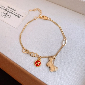 Detail of gold bracelet featuring a red enamel coin charm and a mesh-textured poodle pendant