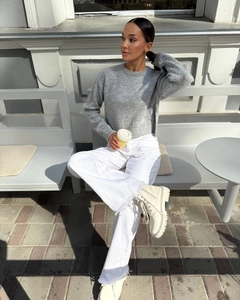 Detail of grey crewneck knit sweater with split hem styled with raw edge white jeans