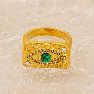Macro detail of gold vintage evil eye ring with green stone and white crystal accents