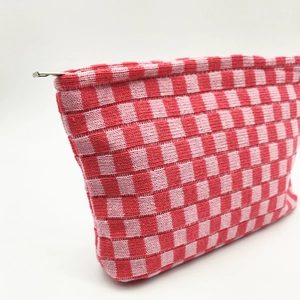 Detail of red and pink gingham knitted makeup bag with silver zipper on white background