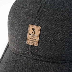 Nahaufnahme von dickem dunkelgrauem Wollstoff und Leder-Logo-Patch auf der Wintermütze