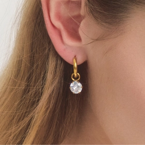Detailed view of a gold hoop earring with a sparkling round zircon pendant worn by a model