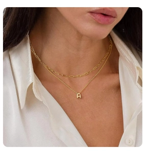 Detail of layered gold paperclip chain and delicate necklace with bubble letter A pendant